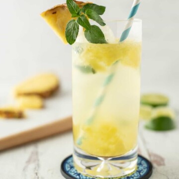 pineapple mojito with blue and white straw and fresh mint and pineapple on the rim