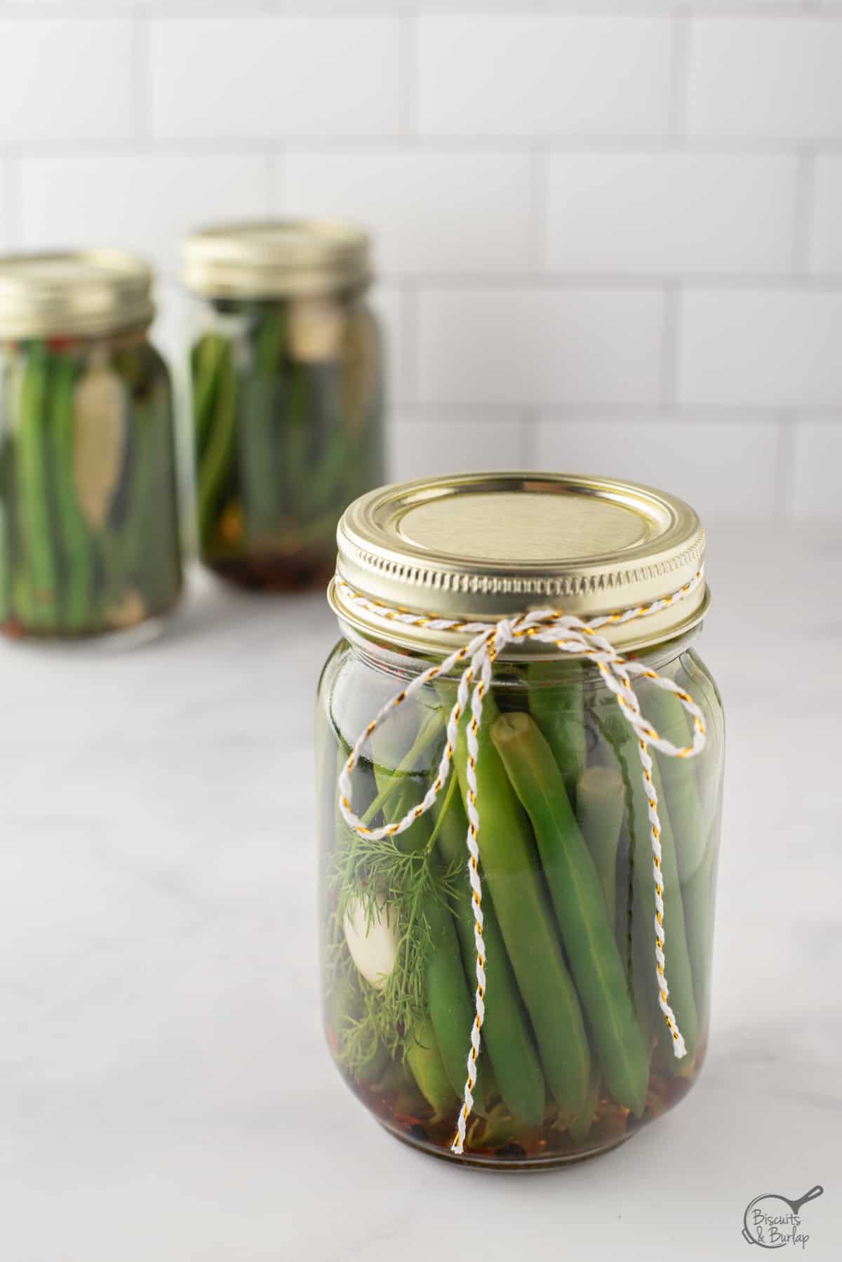 jar of pickled green beans with bow and two more jars behind. 