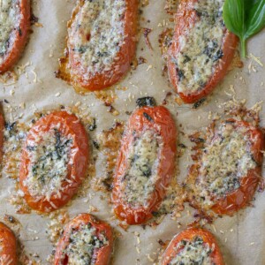 Baked tomato slices with parmesan on parchment paper with fresh basil