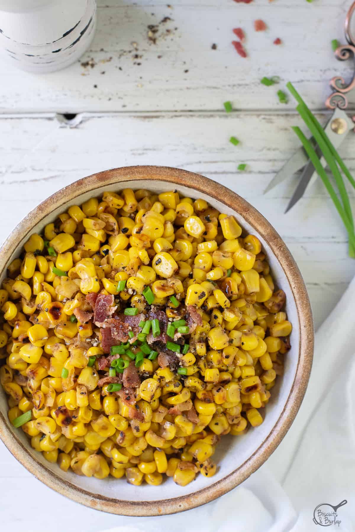 bowl of blackened (charred) corn with shears cutting chives.