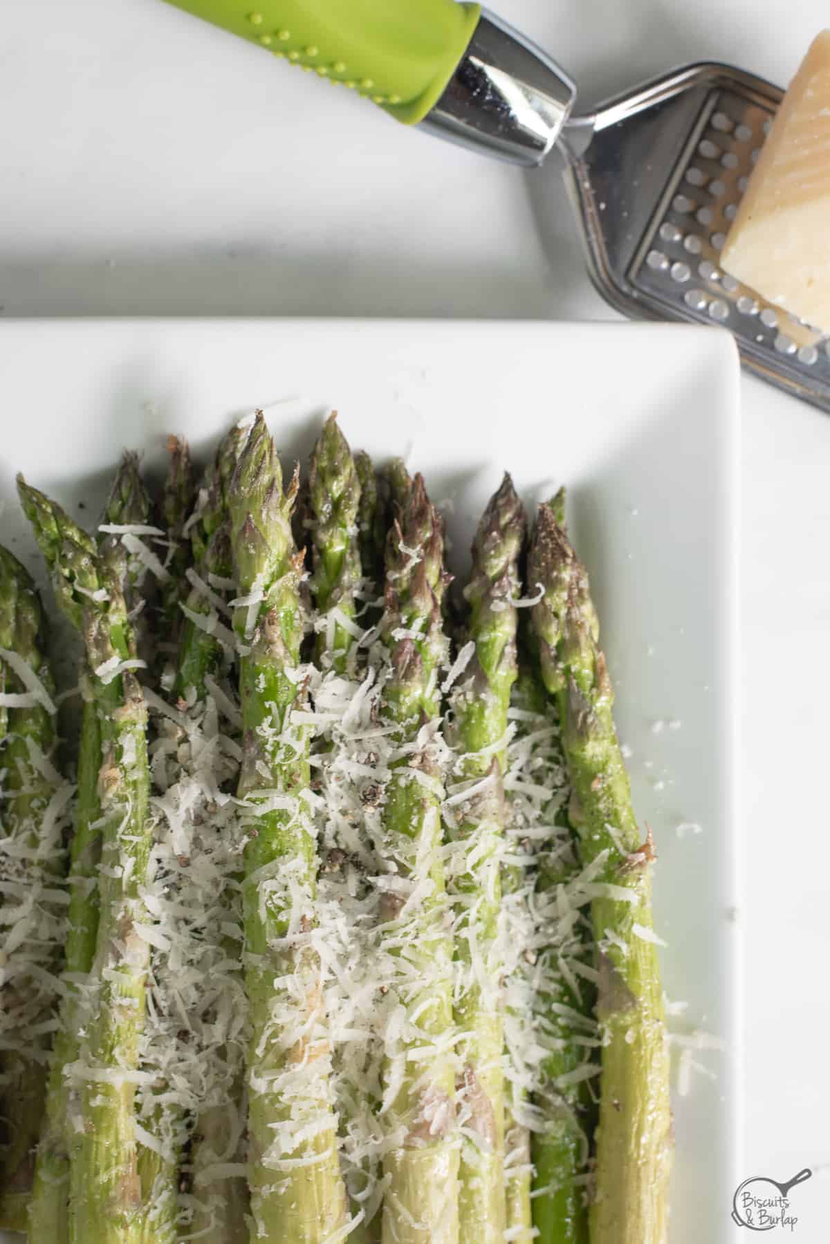 Air Fryer Asparagus Parmesan on white dish with cheese grater and piece of parmesan