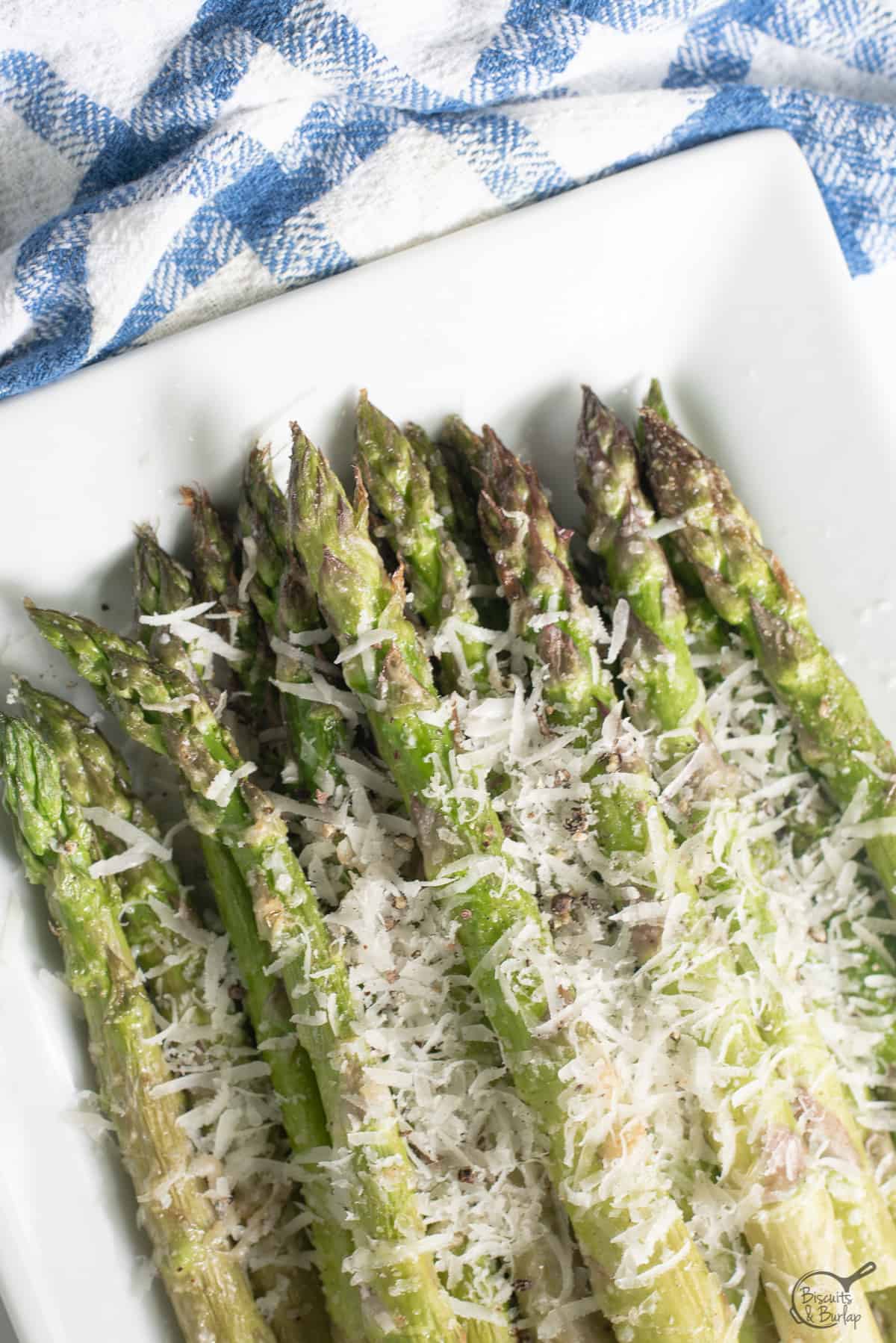 Air Fryer Asparagus Parmesan on a white platter with blue and white checkered fabric
