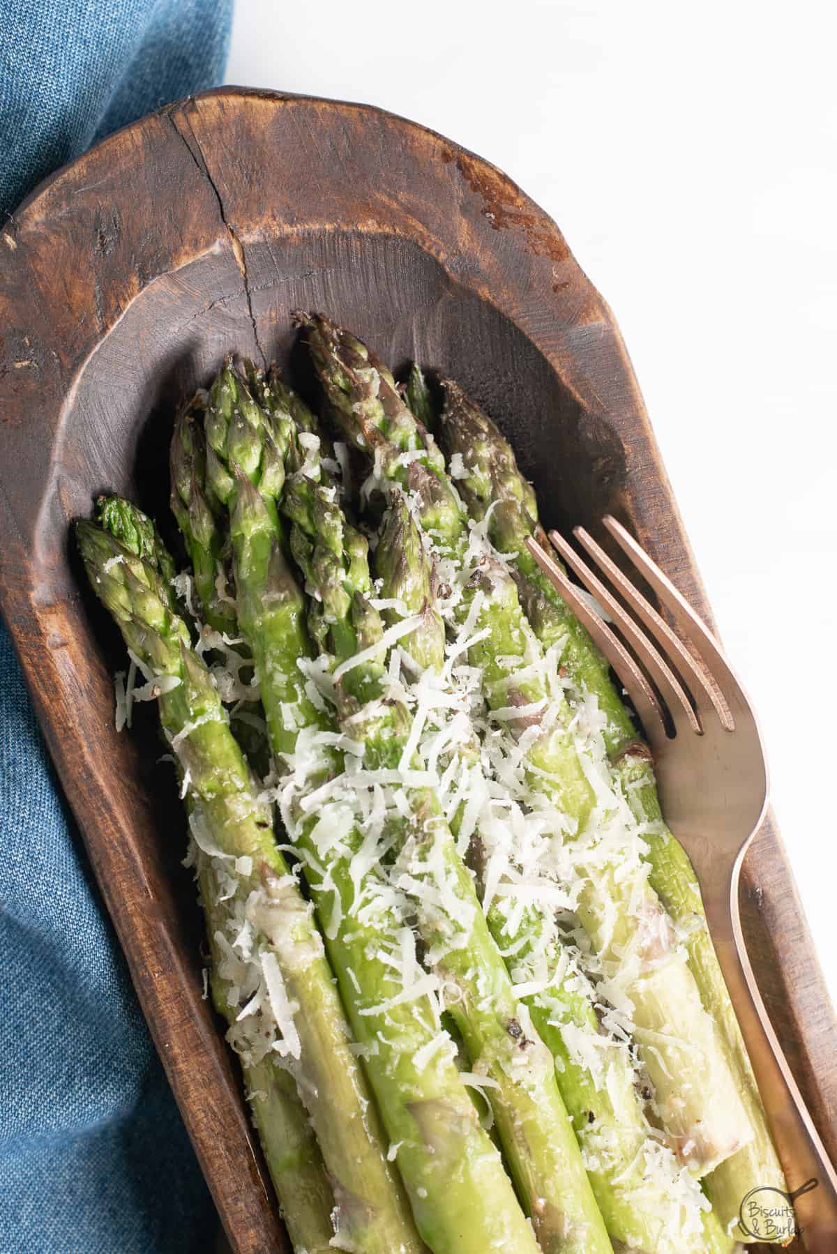 Air Fryer Asparagus Parmesan in wooden dish with a fork and blue fabric