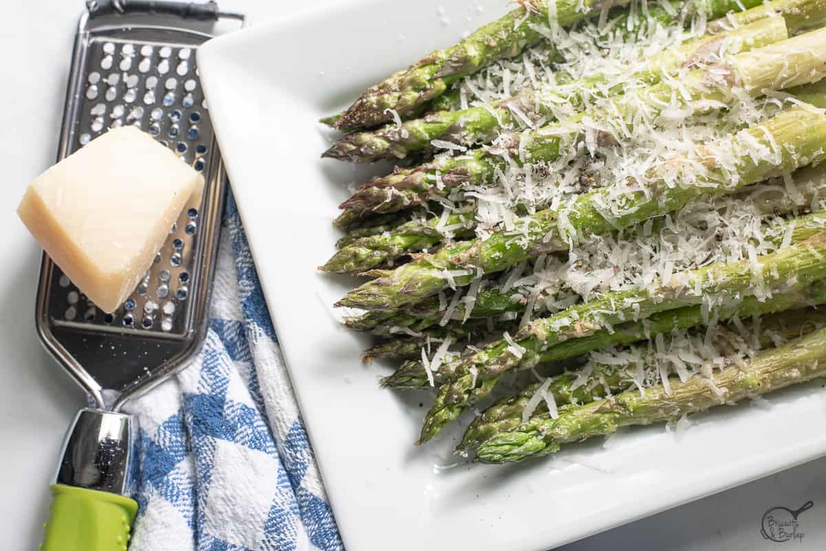 Air Fryer Asparagus Parmesan on white dish with cheese grater and piece of parmesan