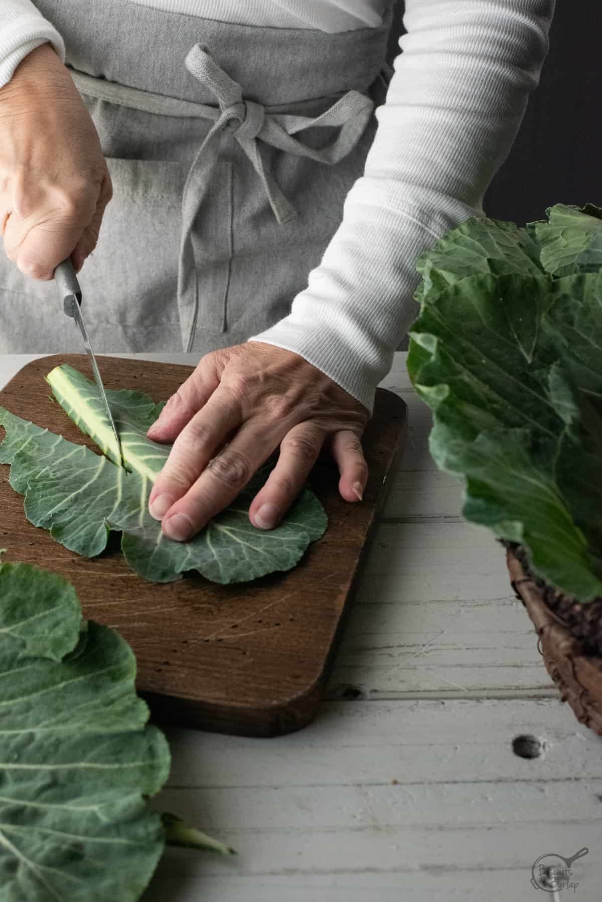 collard green leaf on board being trimmed with knife. 