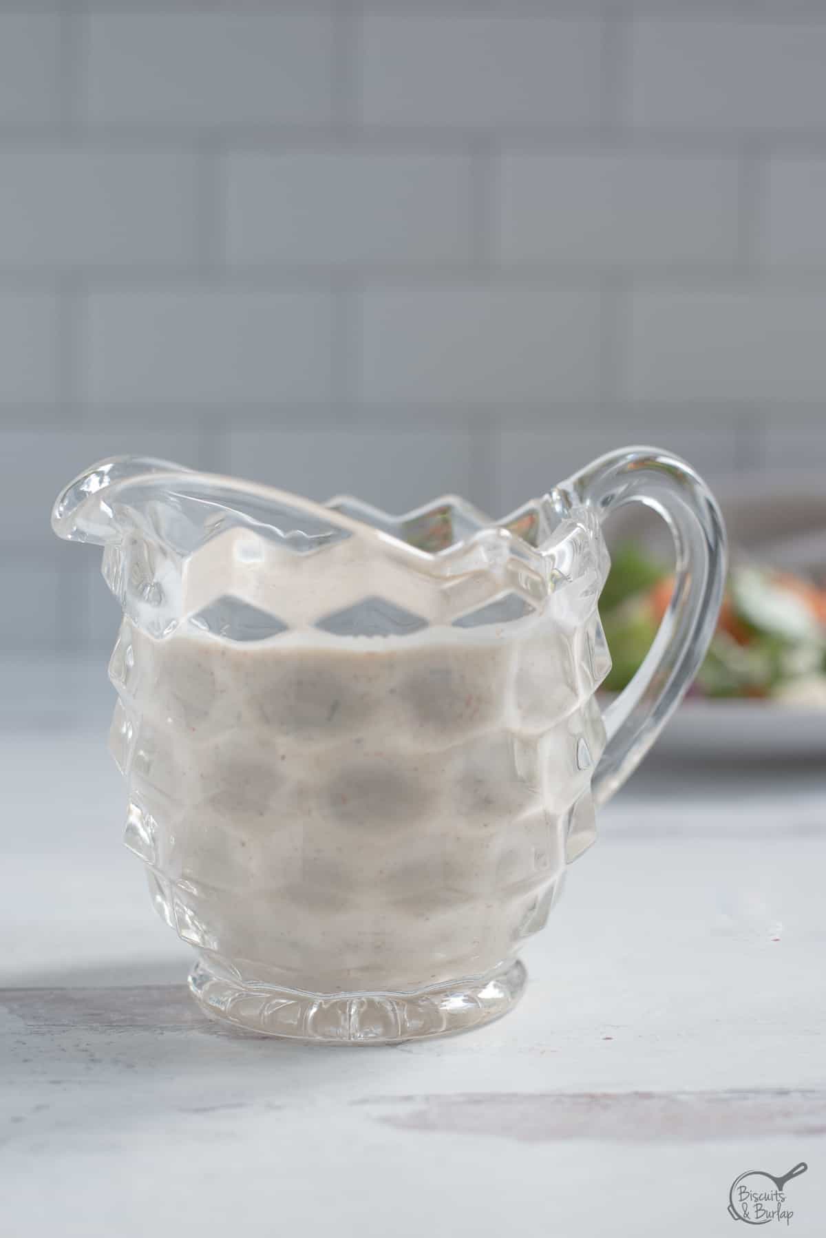 small glass pitcher holding creamy dressing.
