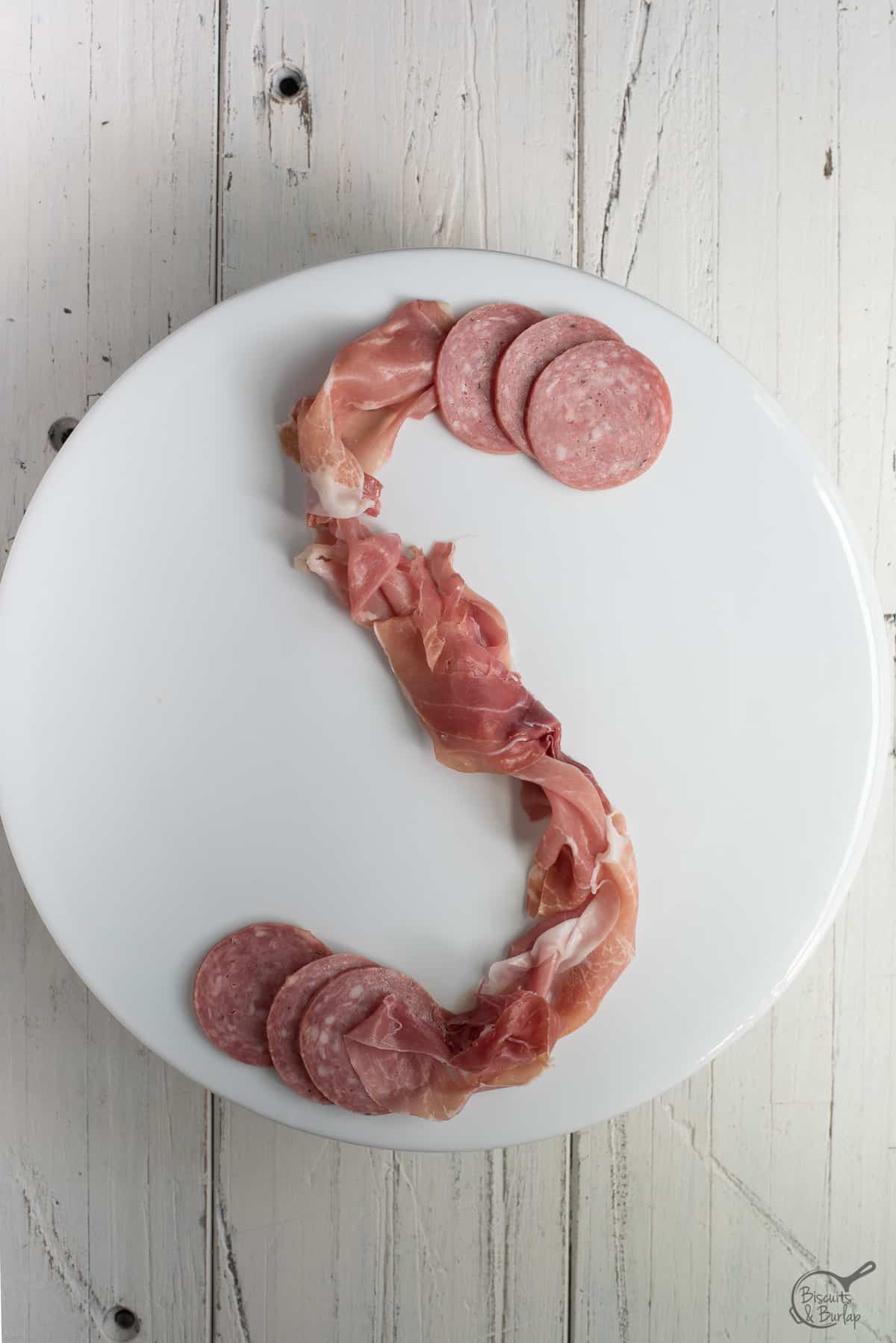 simple charcuterie board being built on white platter on white background