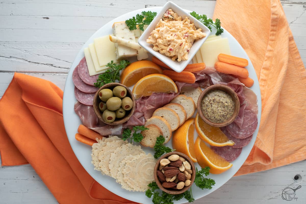 simple charcuterie board on white platter on white background with orange fabric