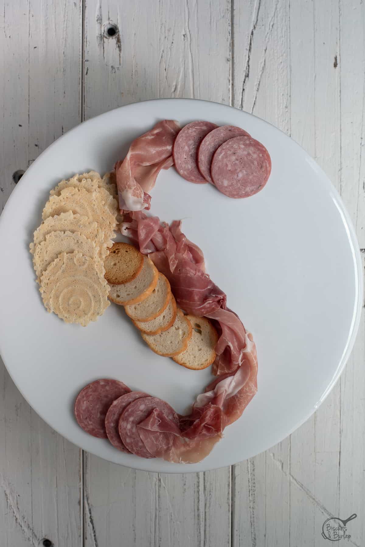 simple charcuterie board being built on white platter on white background