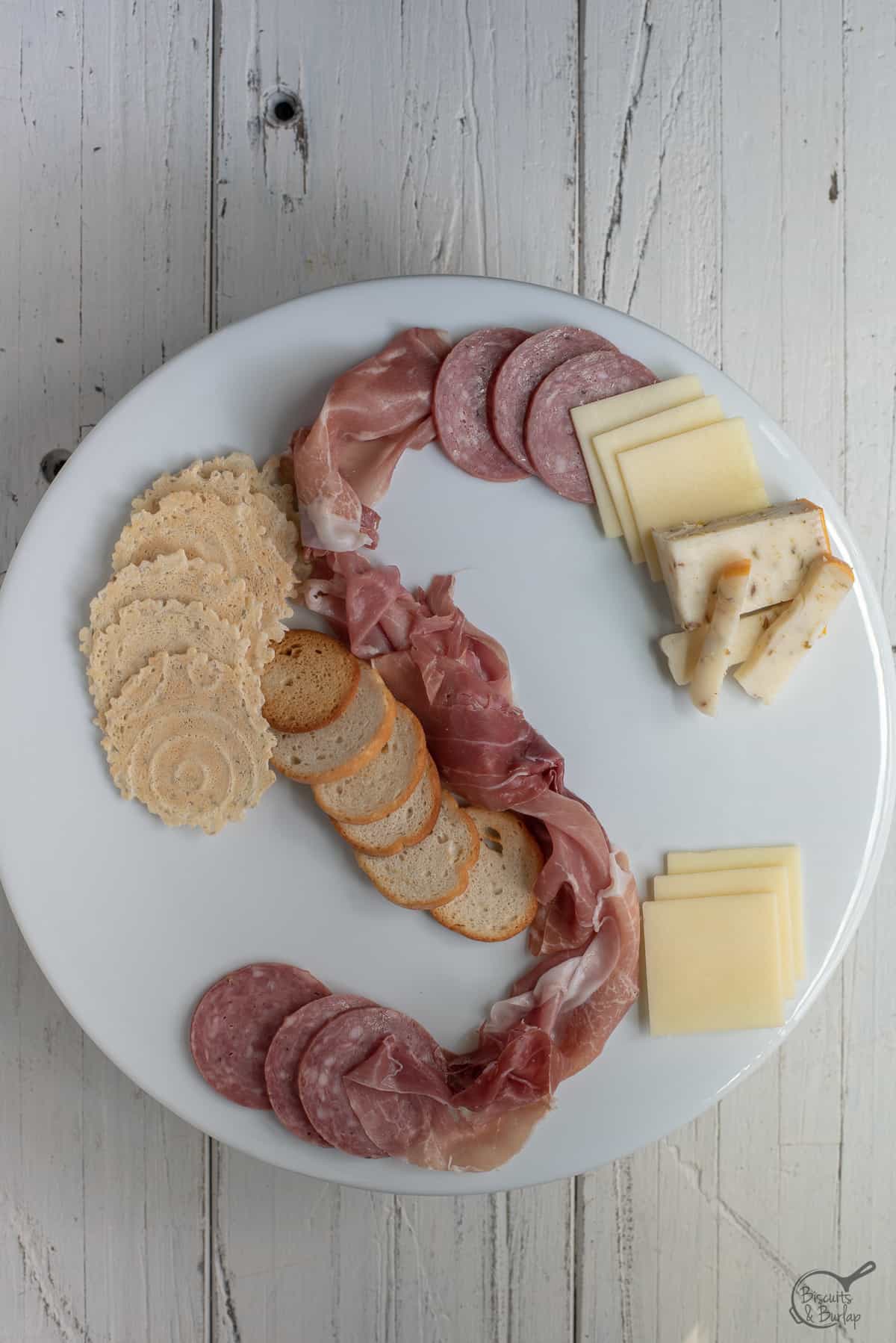 simple charcuterie board being built on white platter on white background