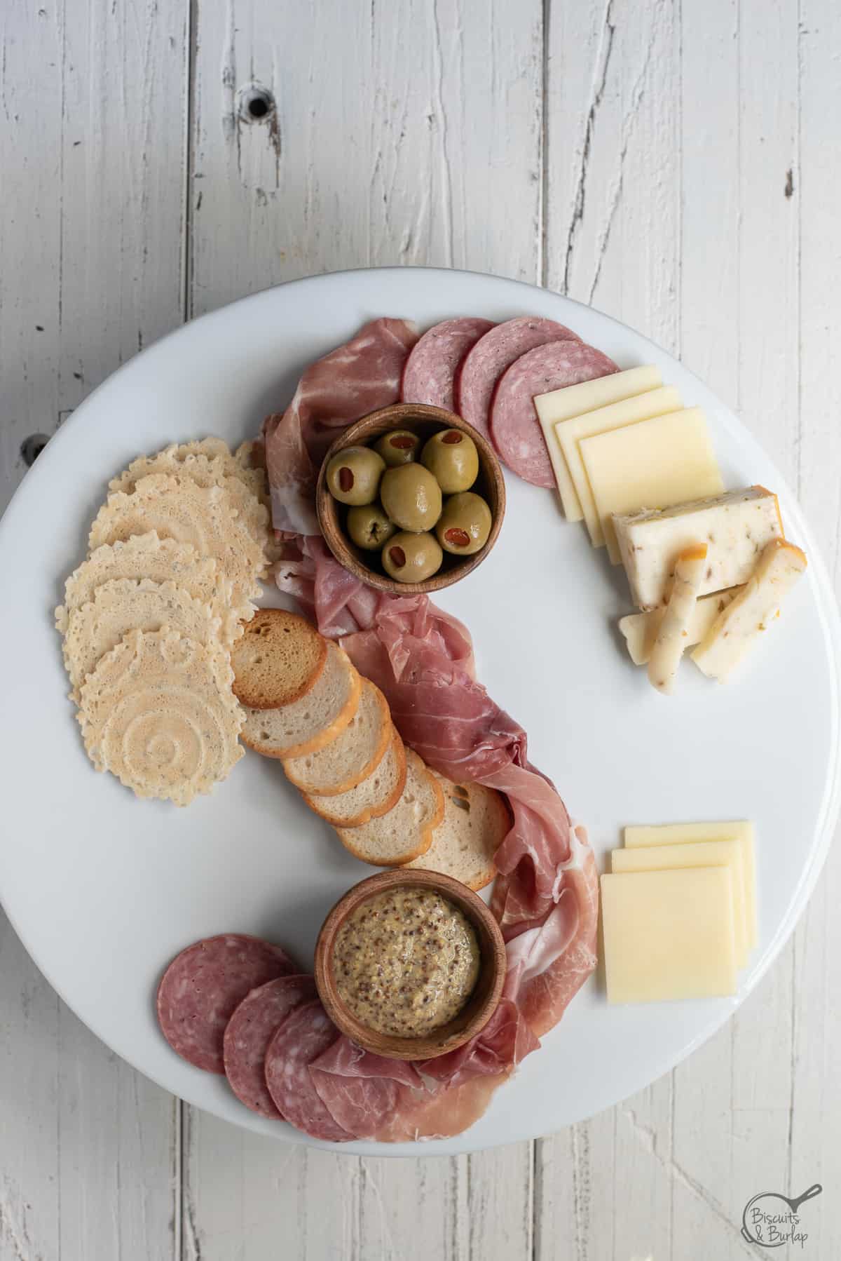 simple charcuterie board being built on white platter on white background