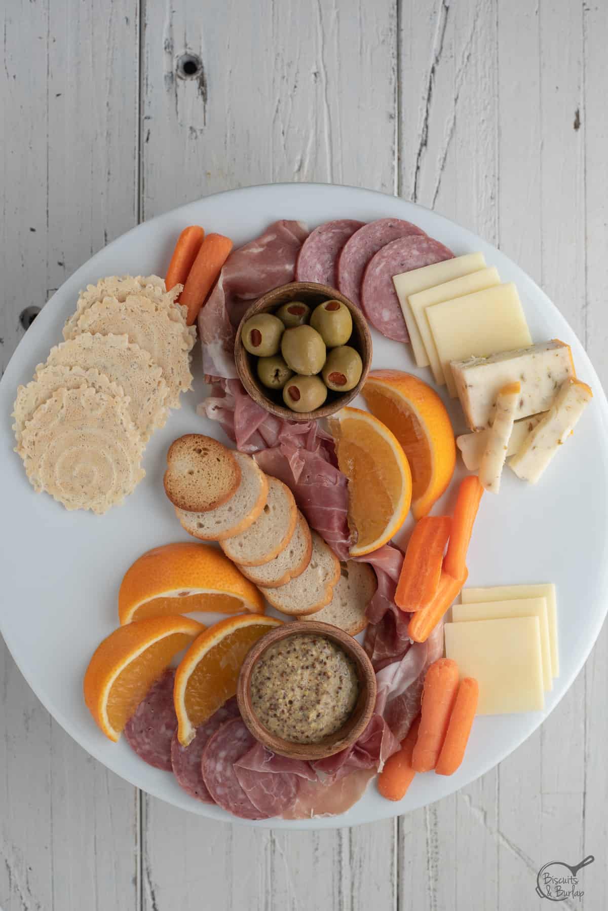 simple charcuterie board being built on white platter on white background