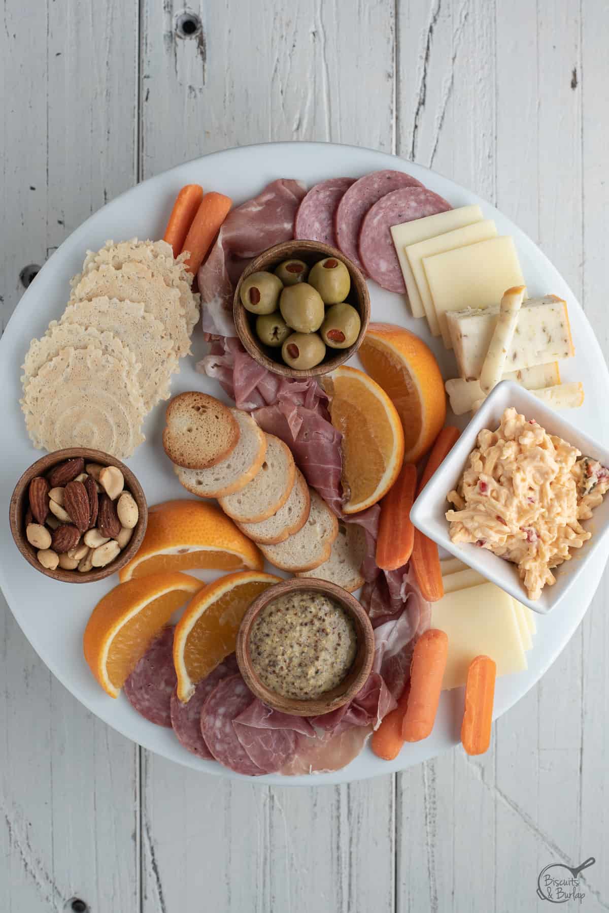 simple charcuterie board being built on white platter on white background