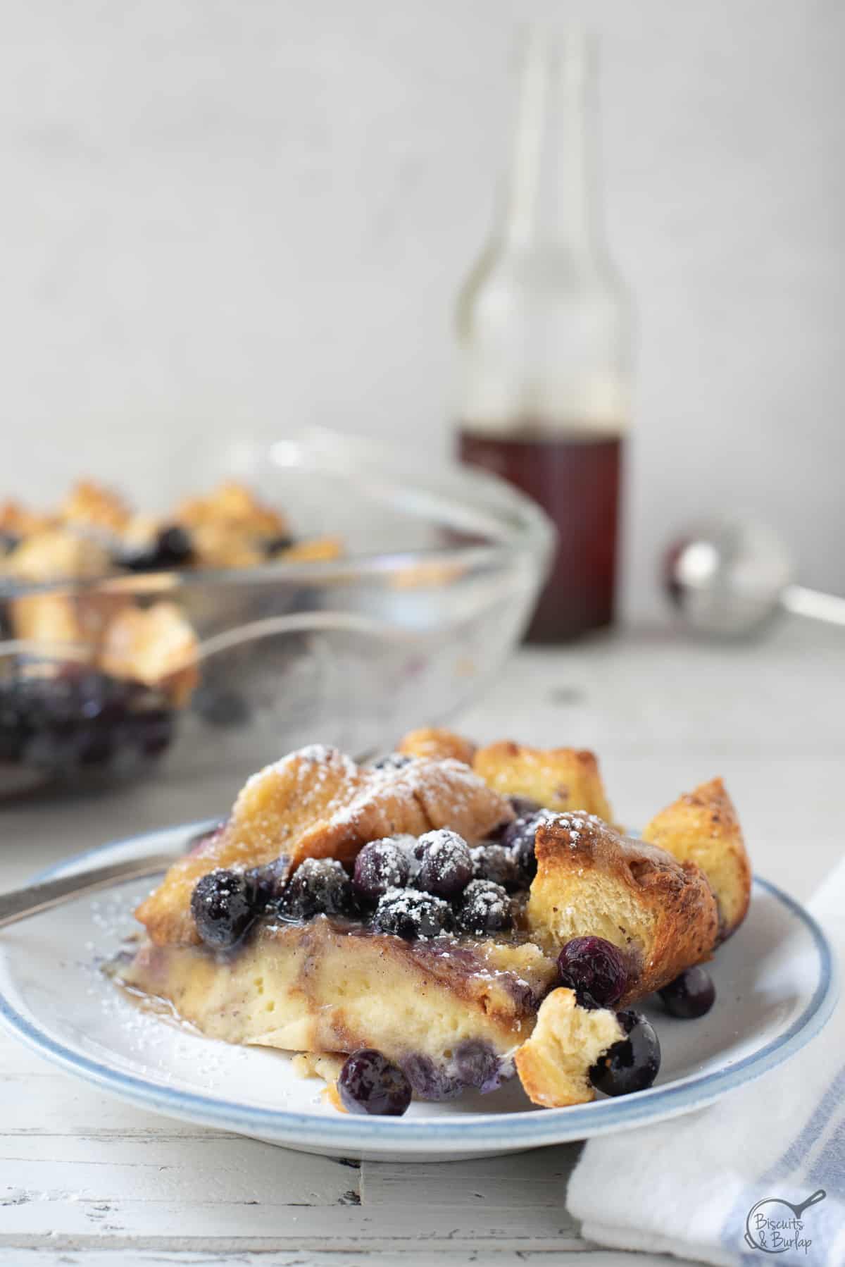 one serving of french toast casserole with syrup behind. 