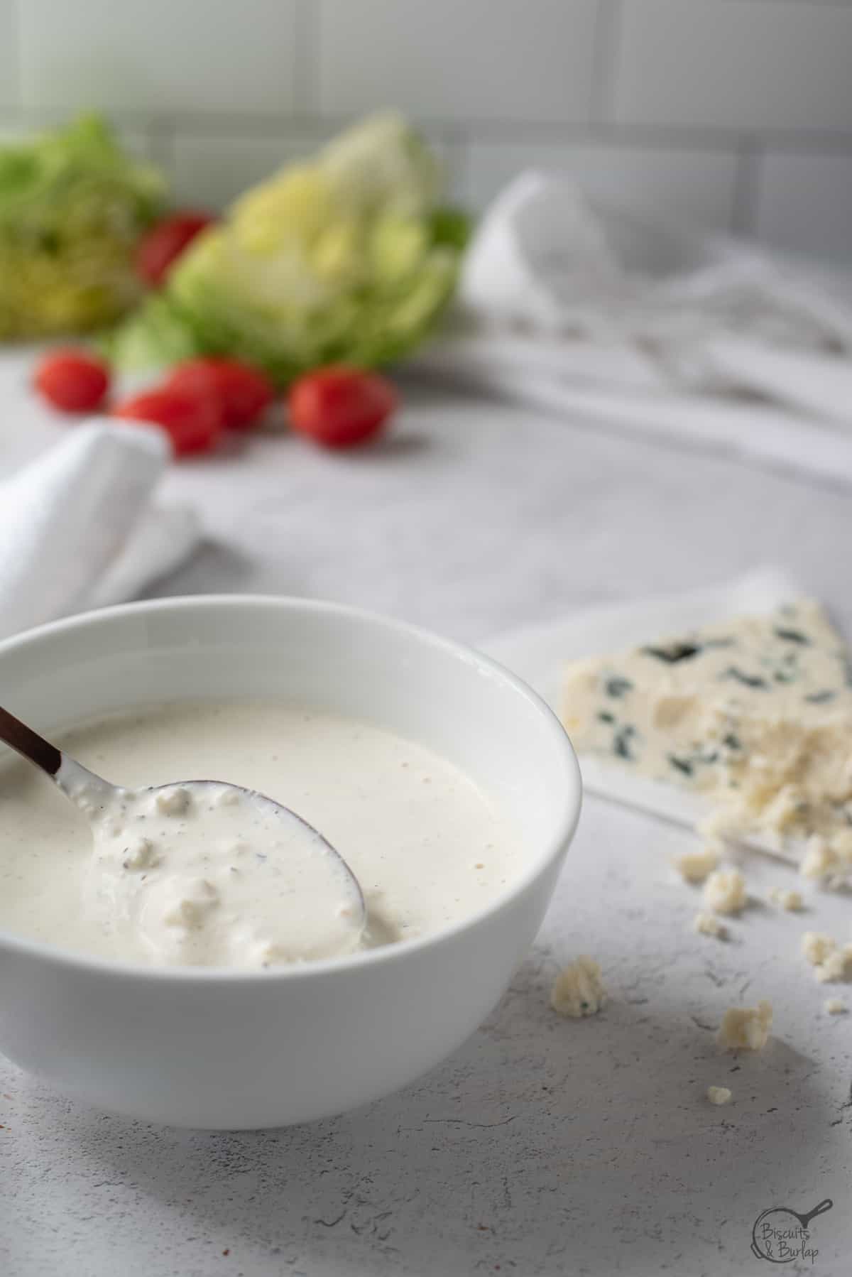 small bowl of Gorgonzola buttermilk dressing with salad ingredients behind. 