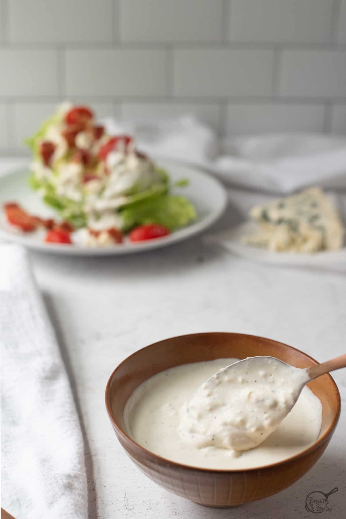 bowl of gorgonzola dressing with wedge salad in back.