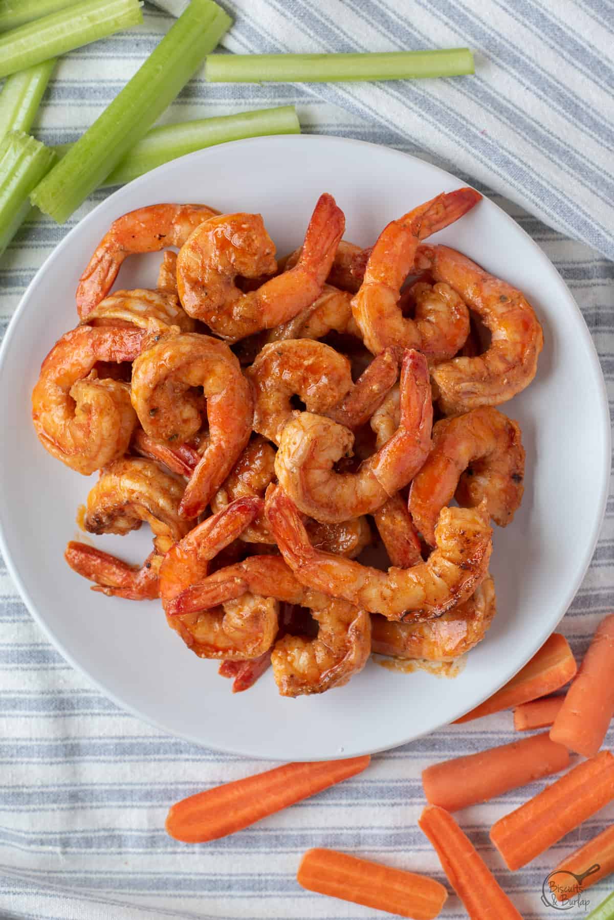 buffalo style shrimp on white plate with celery and carrots. 