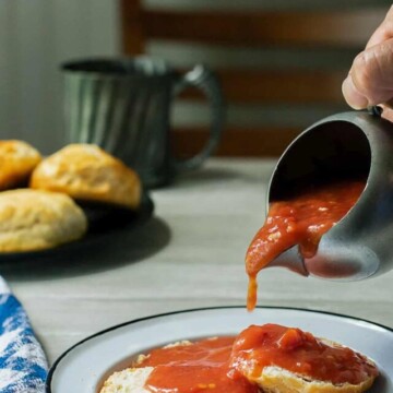 red gravy being poured from small pitcher over biscuits.