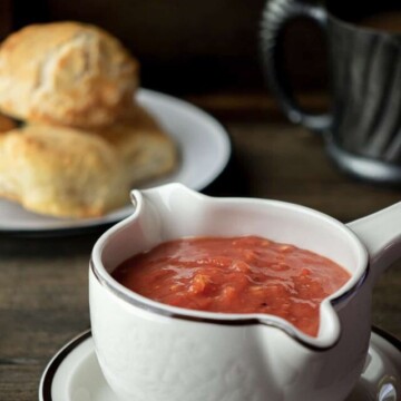 tomato gravy in gravy dish with biscuits behind.