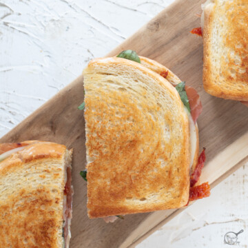 Groumet Grilled cheese, sliced in half on board with white background