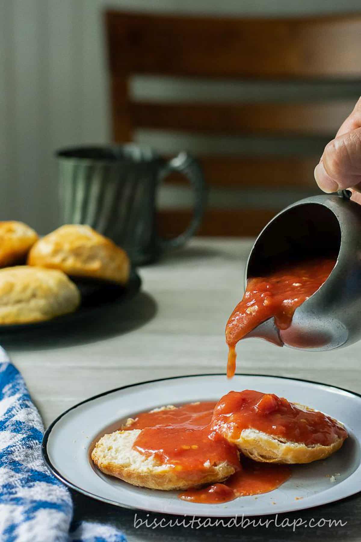 red gravy being poured from small pitcher over biscuits.