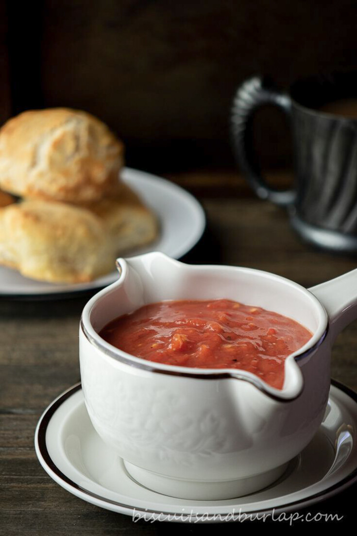 tomato gravy in gravy dish with biscuits behind.