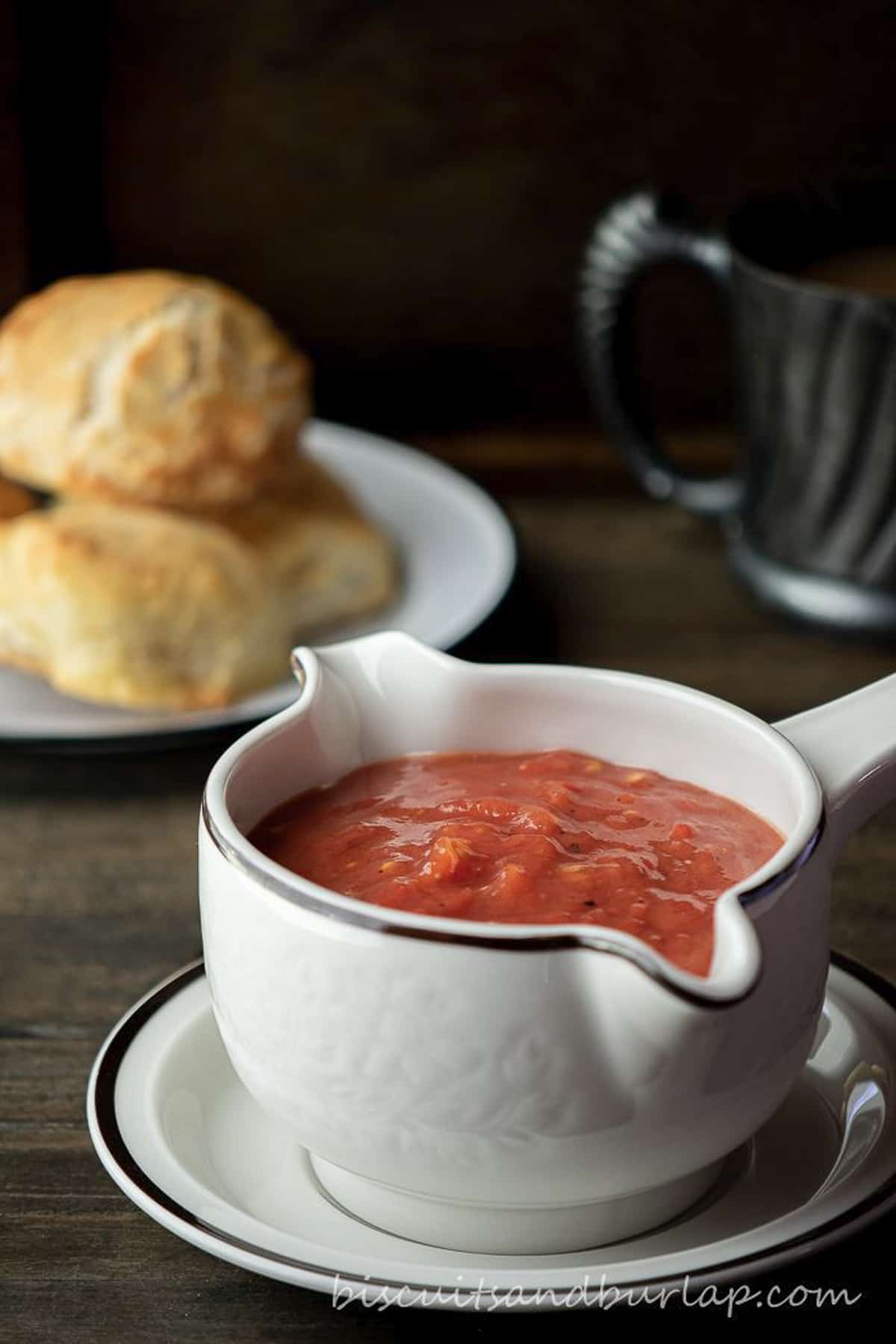 tomato gravy in gravy dish with biscuits behind. 