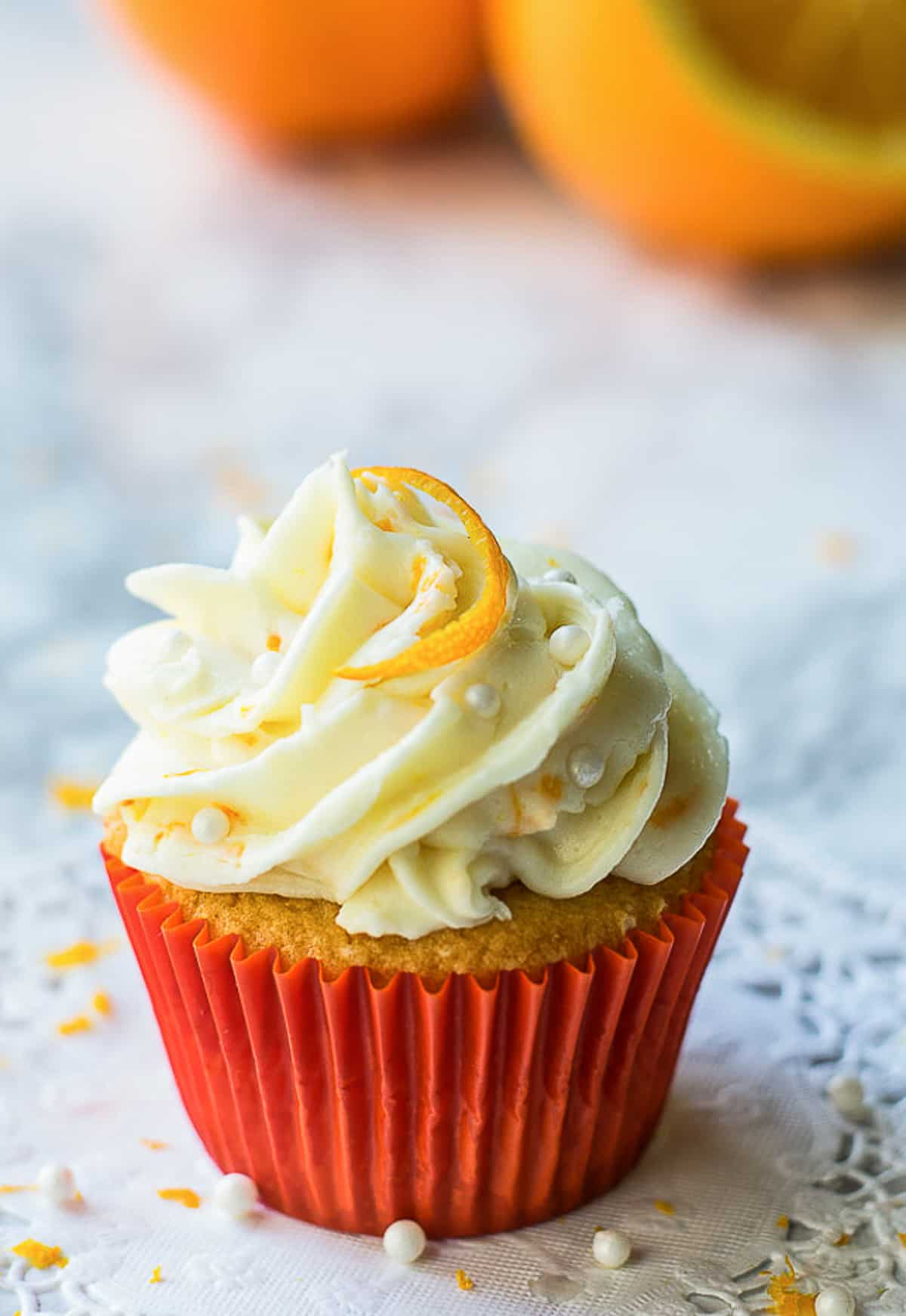 one orange cream cupcake with orange slices behind. 