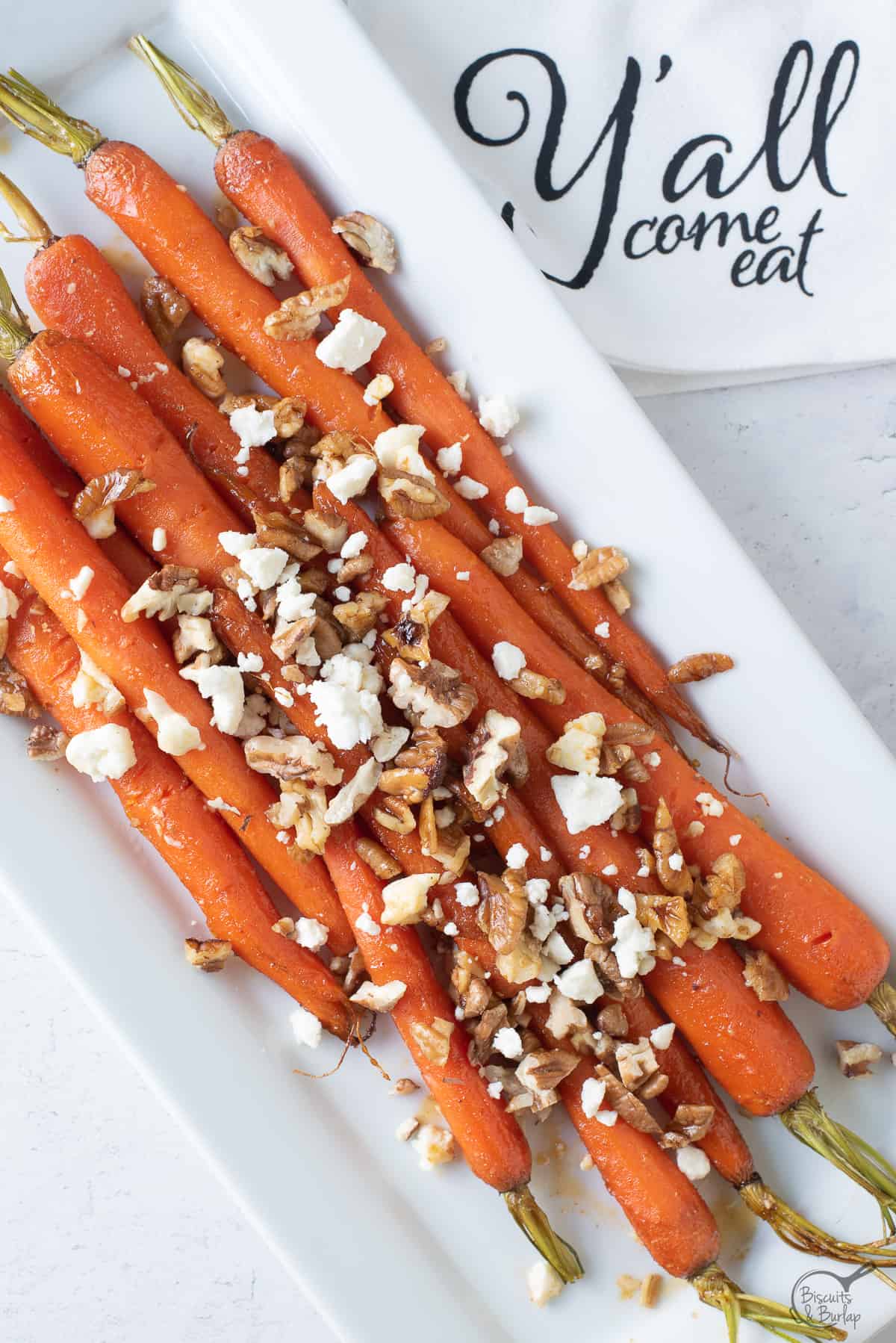 Brown sugar honey glazed carrots on dish with "y'all come eat" towel.