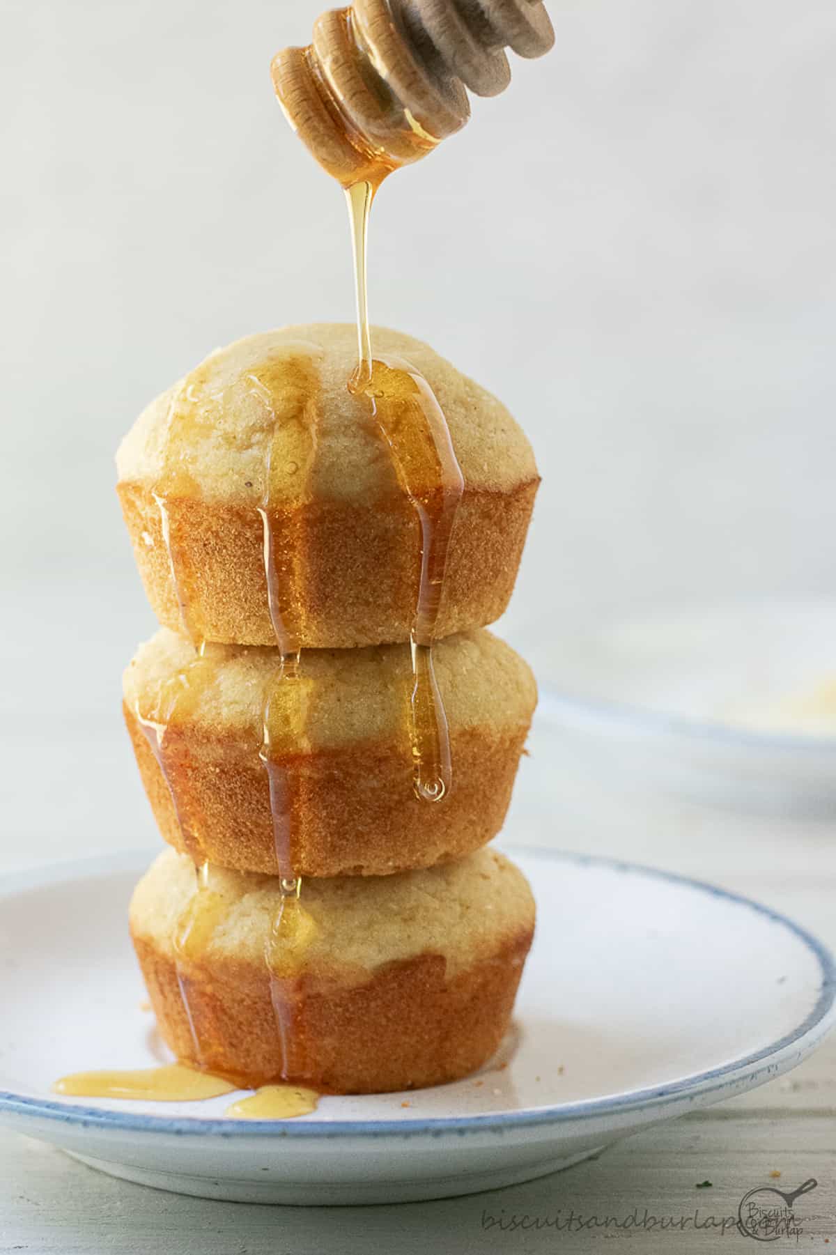 stack of 3 cornbread muffins with honey running down sides.