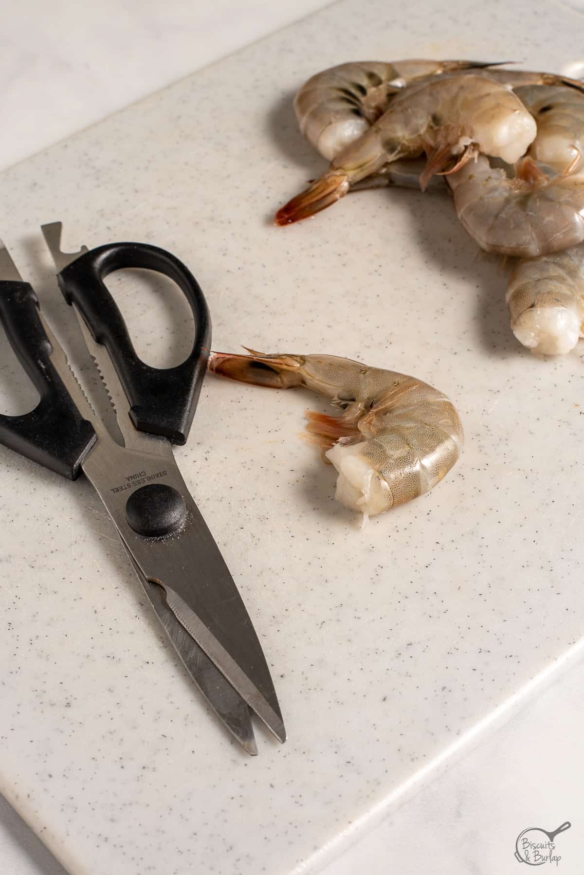 kitchen shears and raw shrimp on cutting board. 