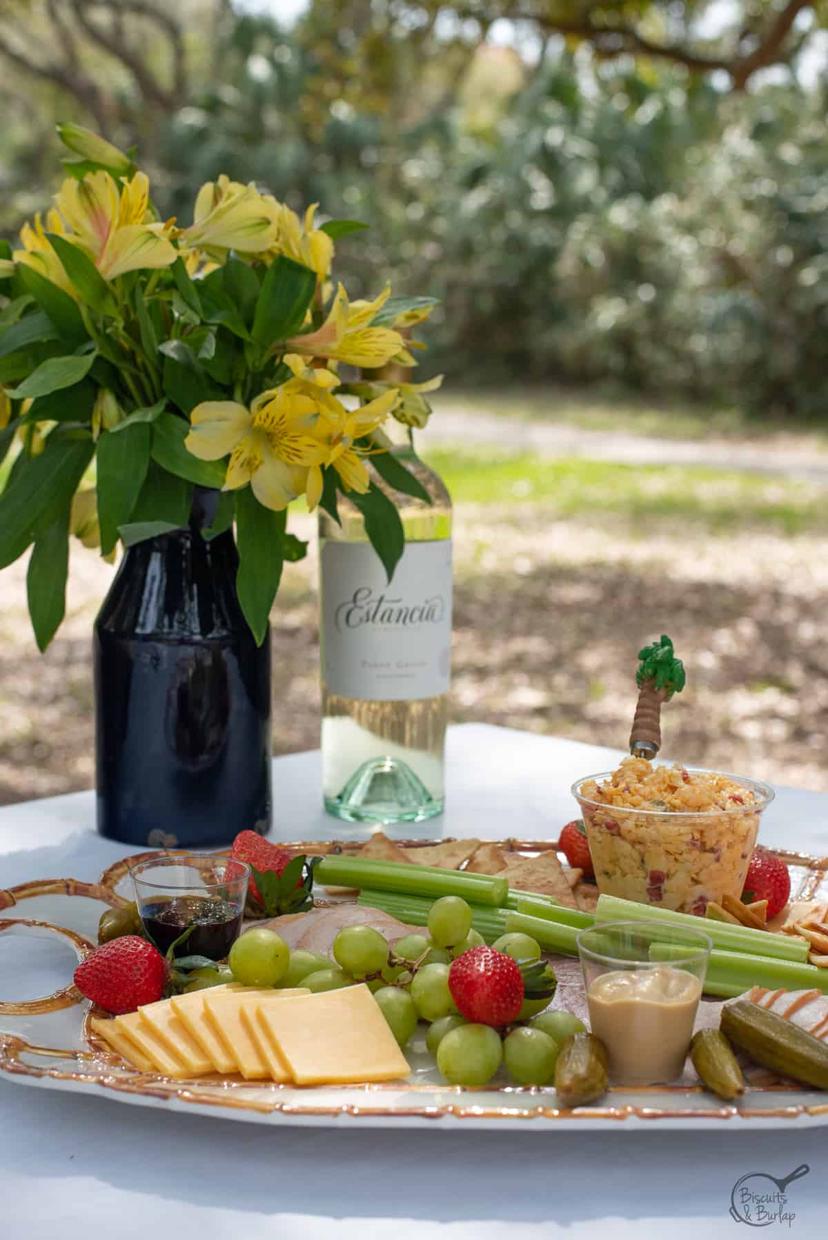 charcuterie board on picnic table with flowers and wine. 