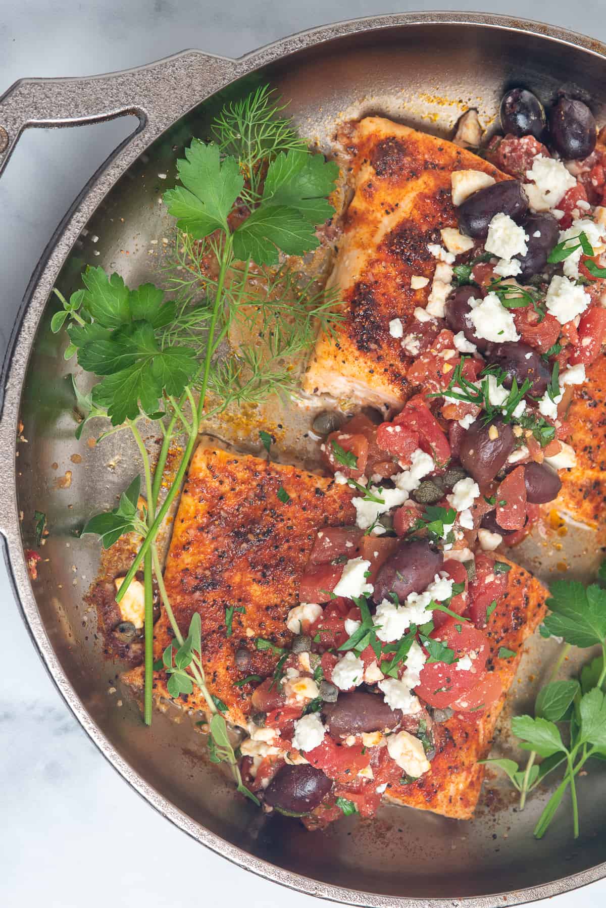 Salmon fillets in skillet with herbs and greek topping. 