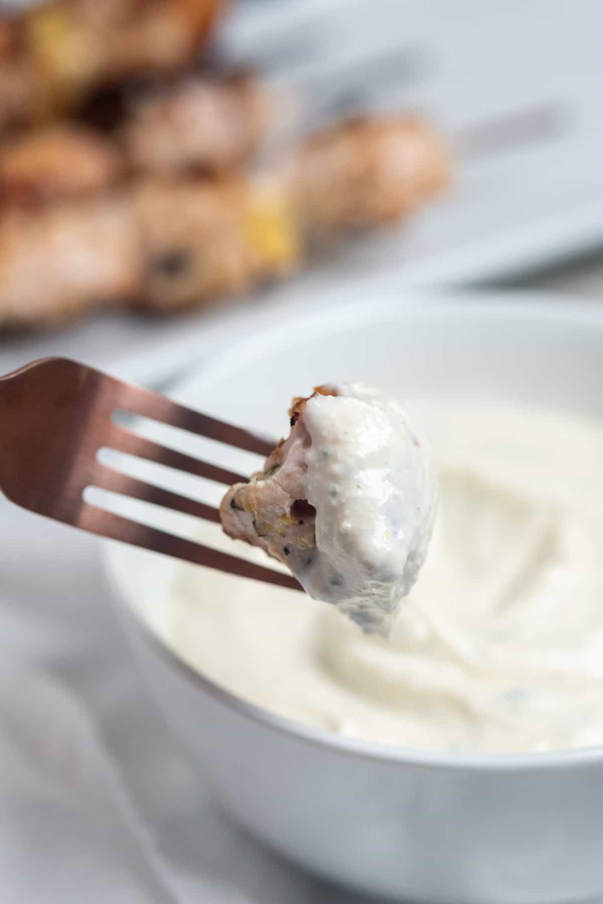 piece of chicken being dipped in lemon yogurt sauce. 