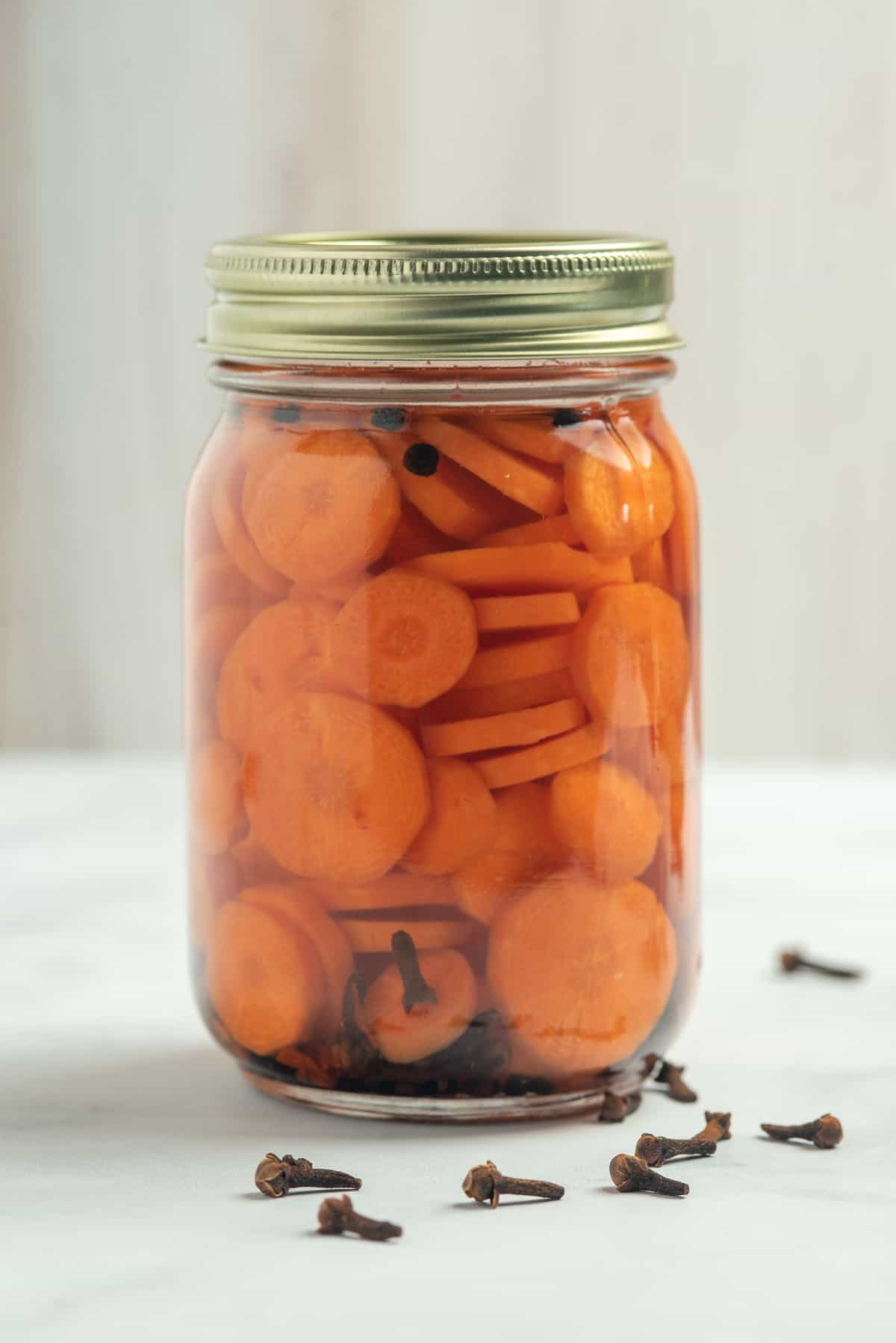 jar of pickled carrots with cloves around. 