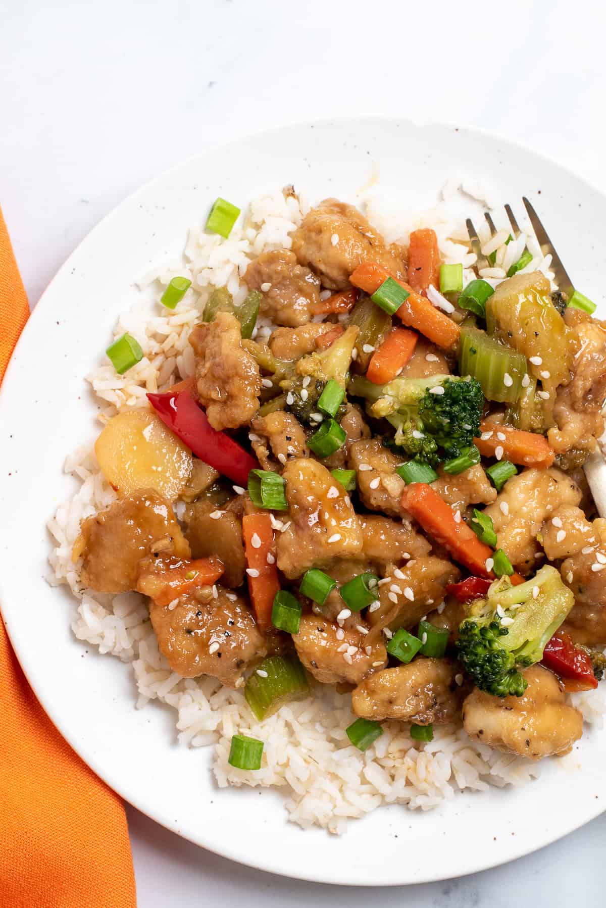 Honey bourbon chicken on white plate with fork and orange napkin