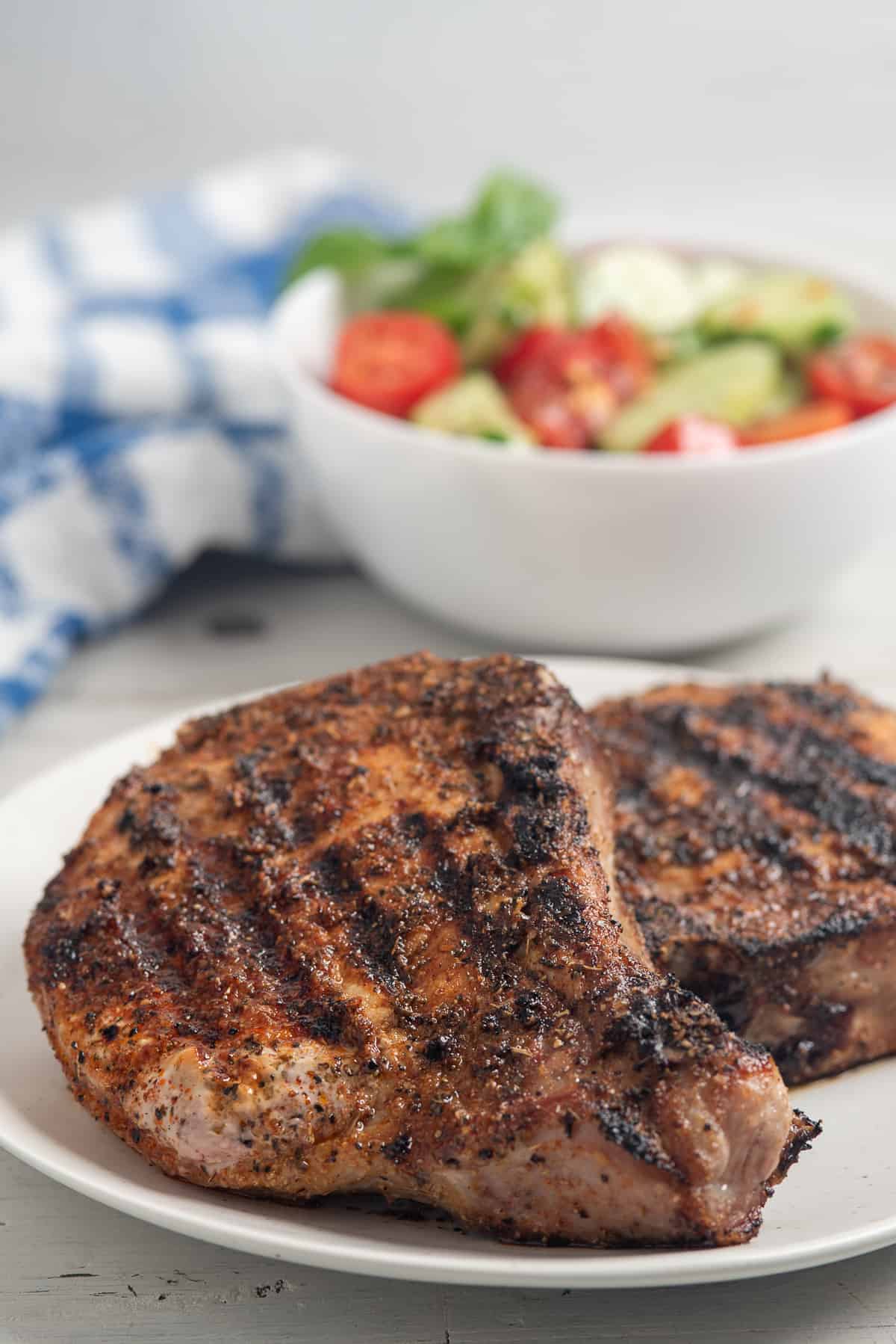 blackend pork chops with salad behind. 