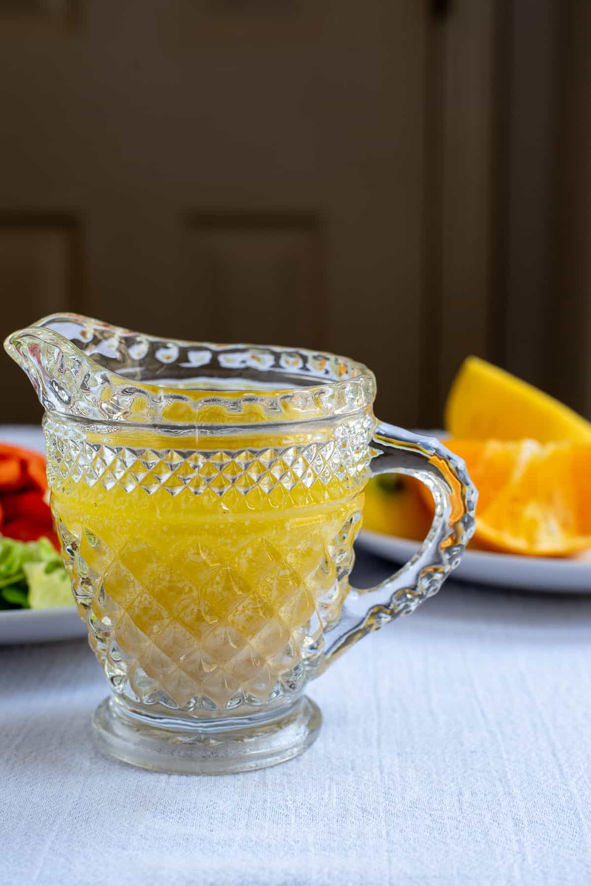 citrus salad dressing in glass pitcher with oranges in background