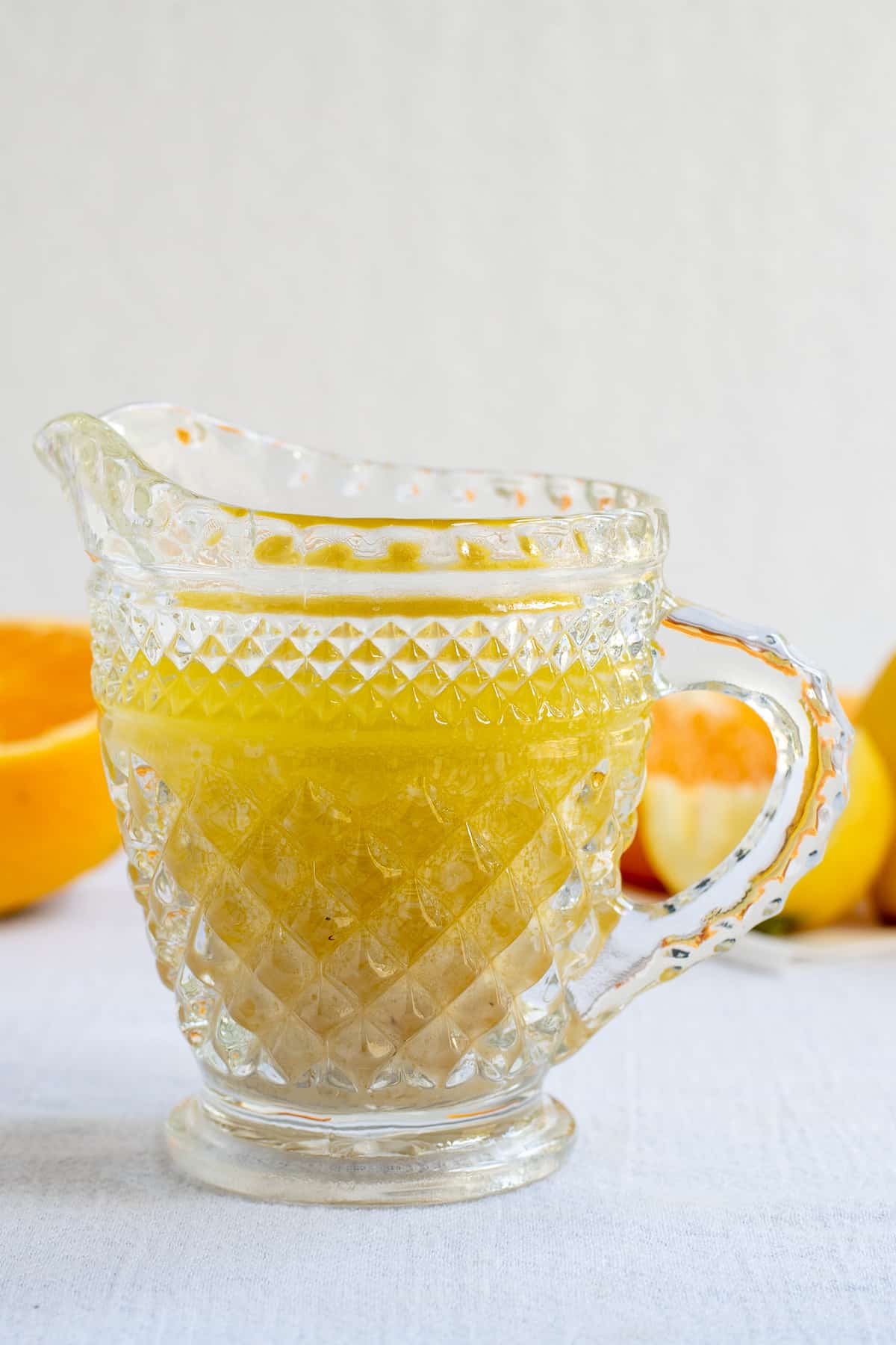 citrus salad dressing in glass pitcher on white background with oranges