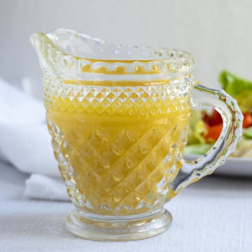 citrus salad dressing in glass pitcher with salad in background