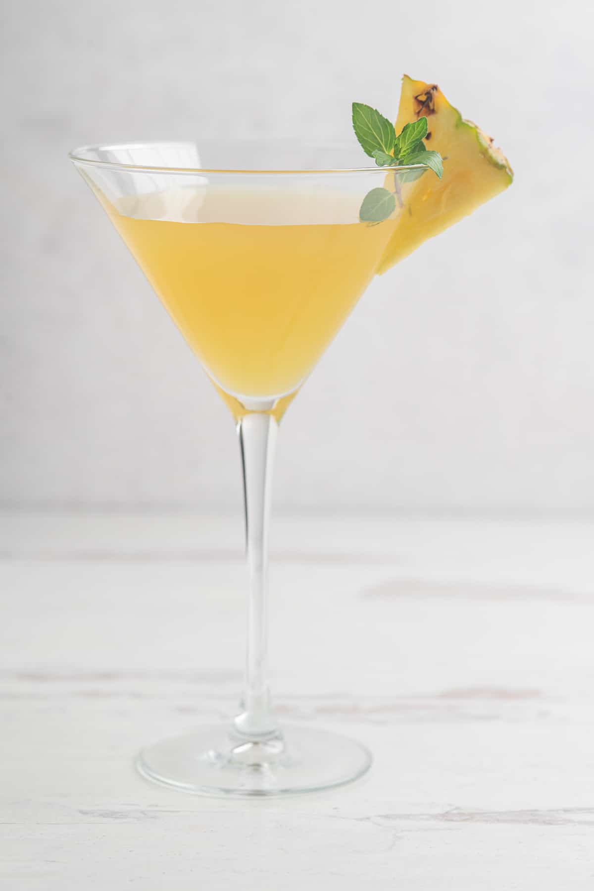 cocktail made with pineapple agua fresca in a martini glass garnished with fresh pineapple and mint on a white background