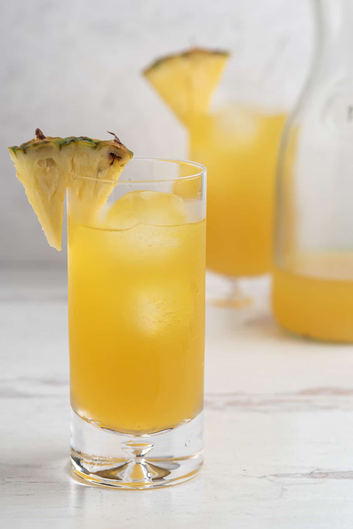 Tall, skinny glass of pineapple agua fresca with a fresh pineapple garnish on a white background
