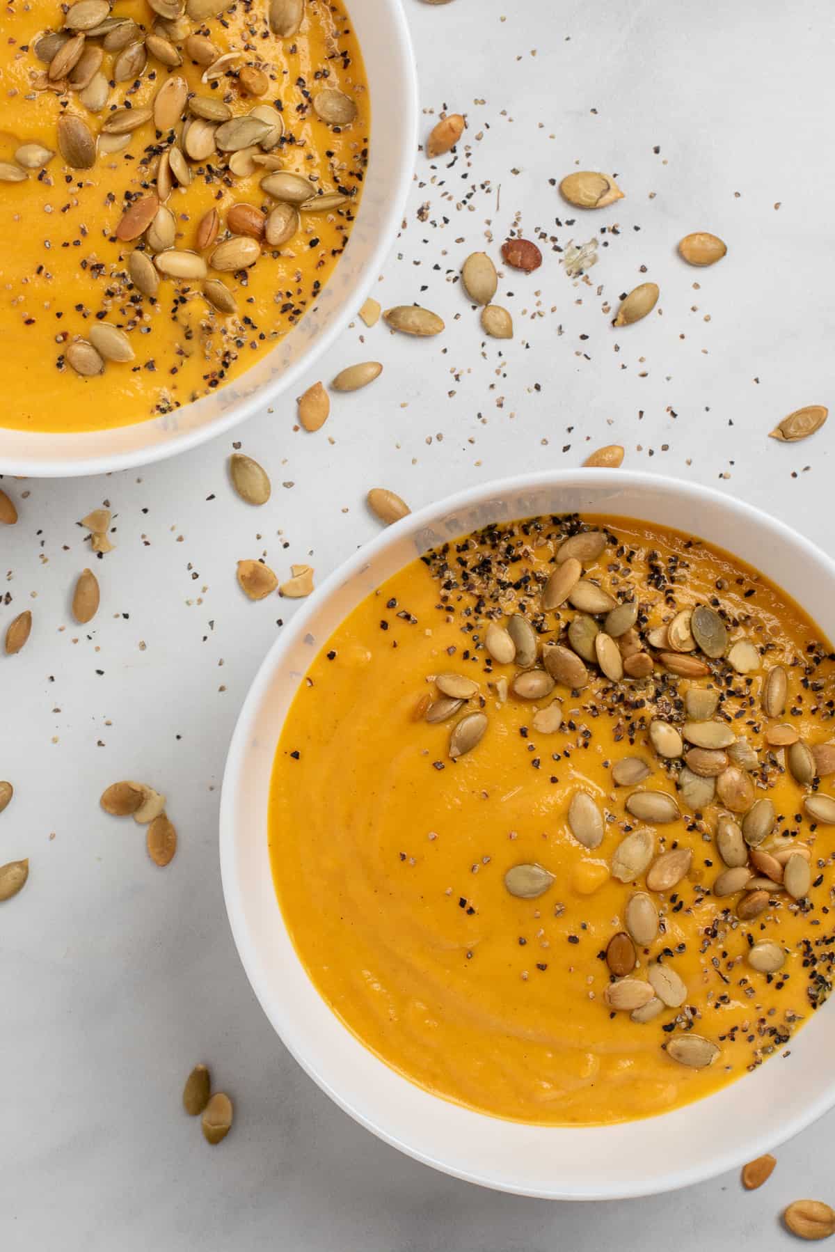 2 bowls of carrot and pumpkin soup with garnish.