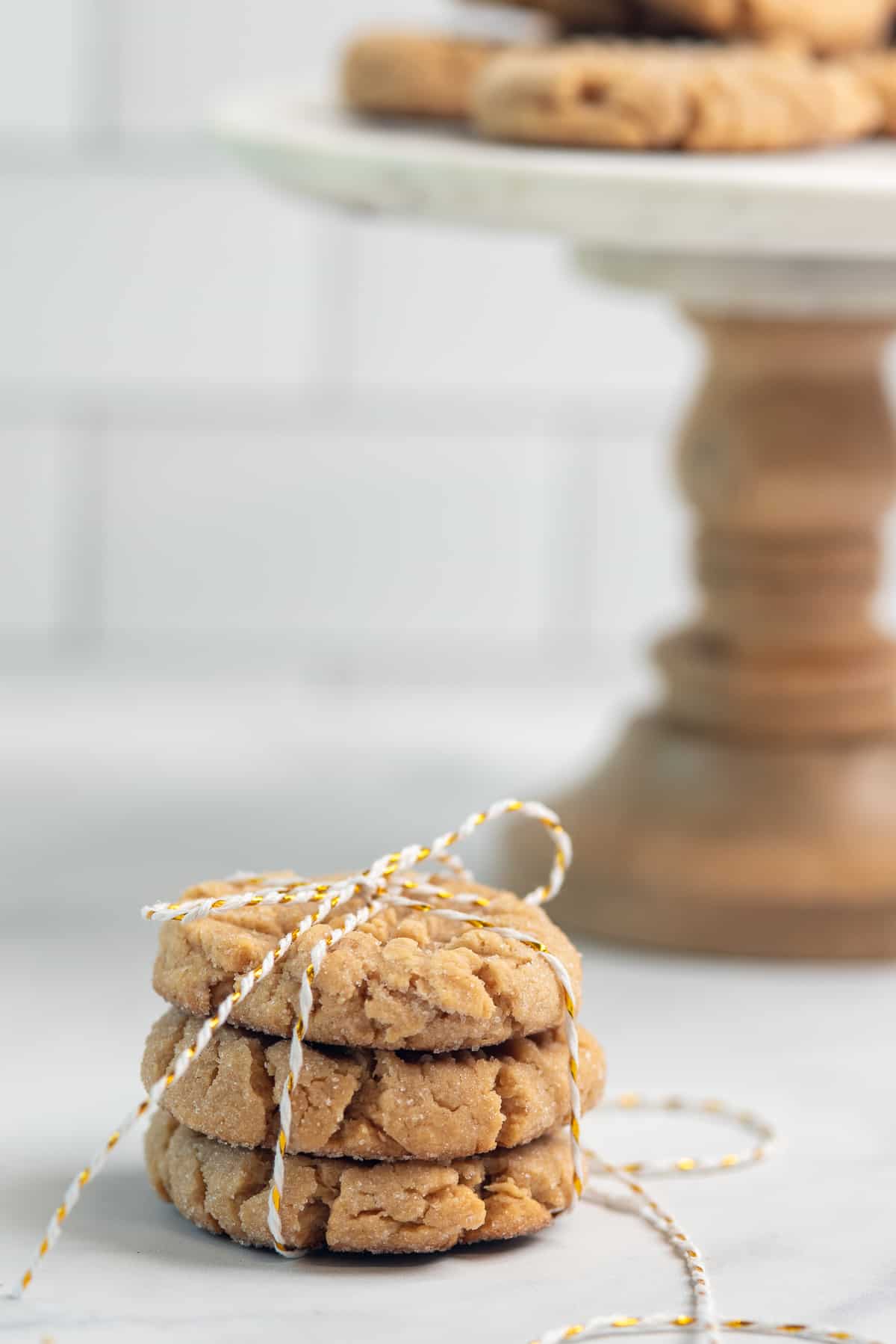 cookies tied up with a ribbon with a cake stand of cookies in the background.