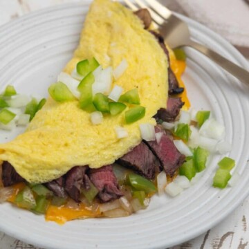omelette stuffed with steak, cheese, peppers, onions, and mushrooms on a white plate