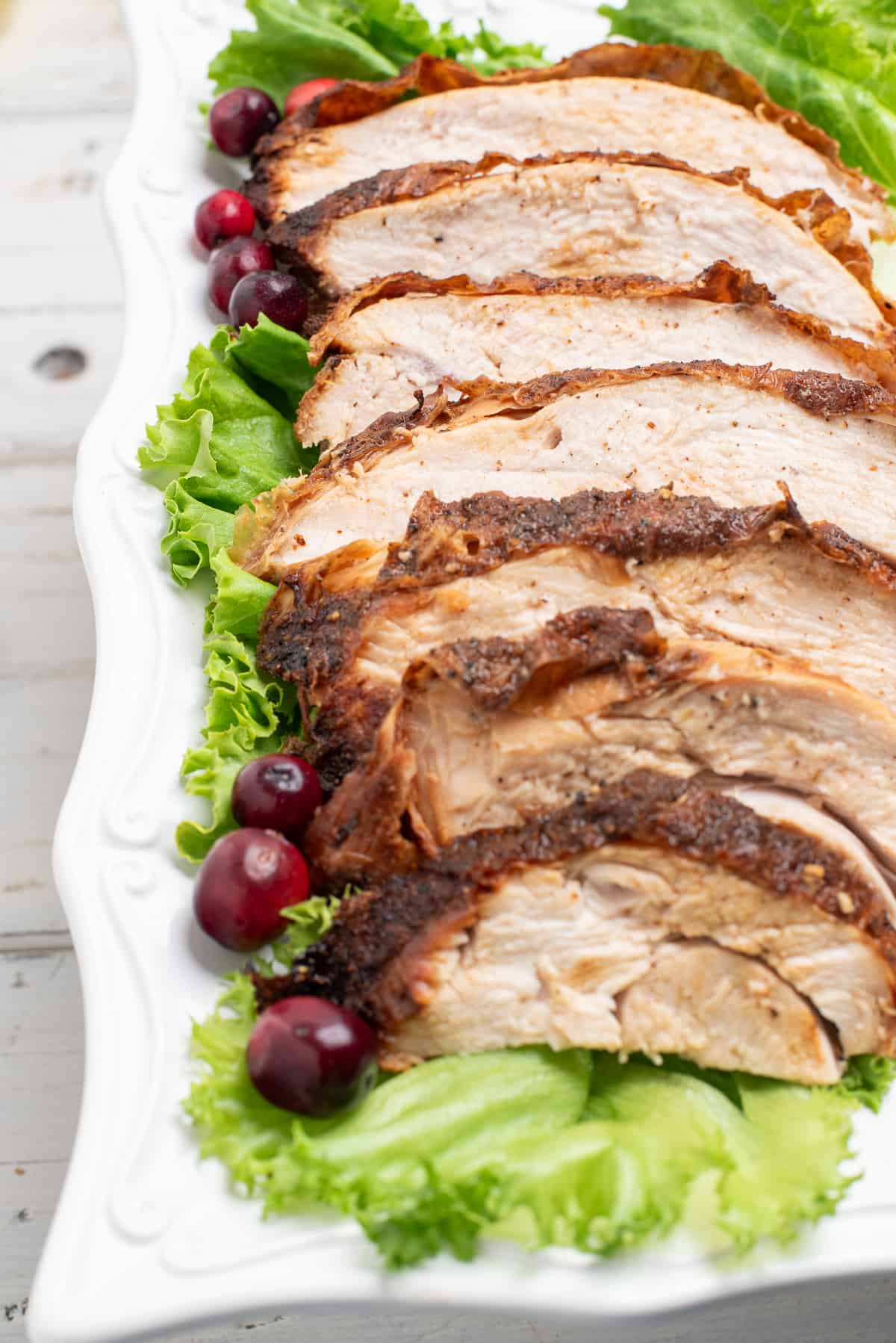 sliced turkey breast on a white plate surrounded by lettuce and cranberries