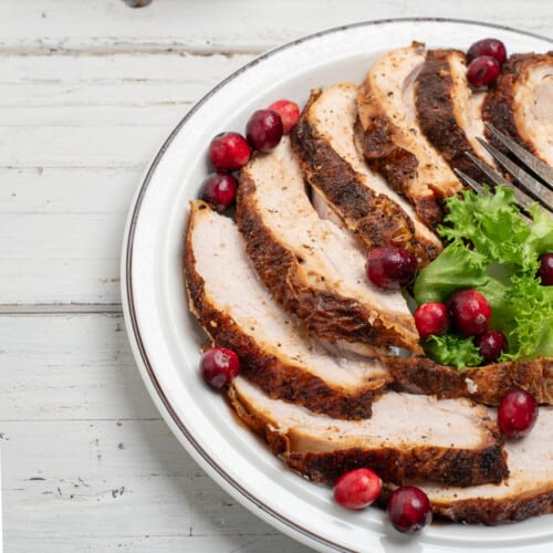 sliced cajun fried turkey breast on a white plate with a white background