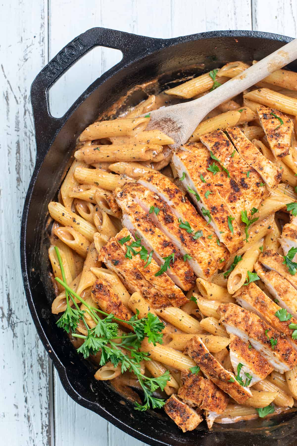 chicken pasta in a cast iron skillet with a spoon and fresh parsley
