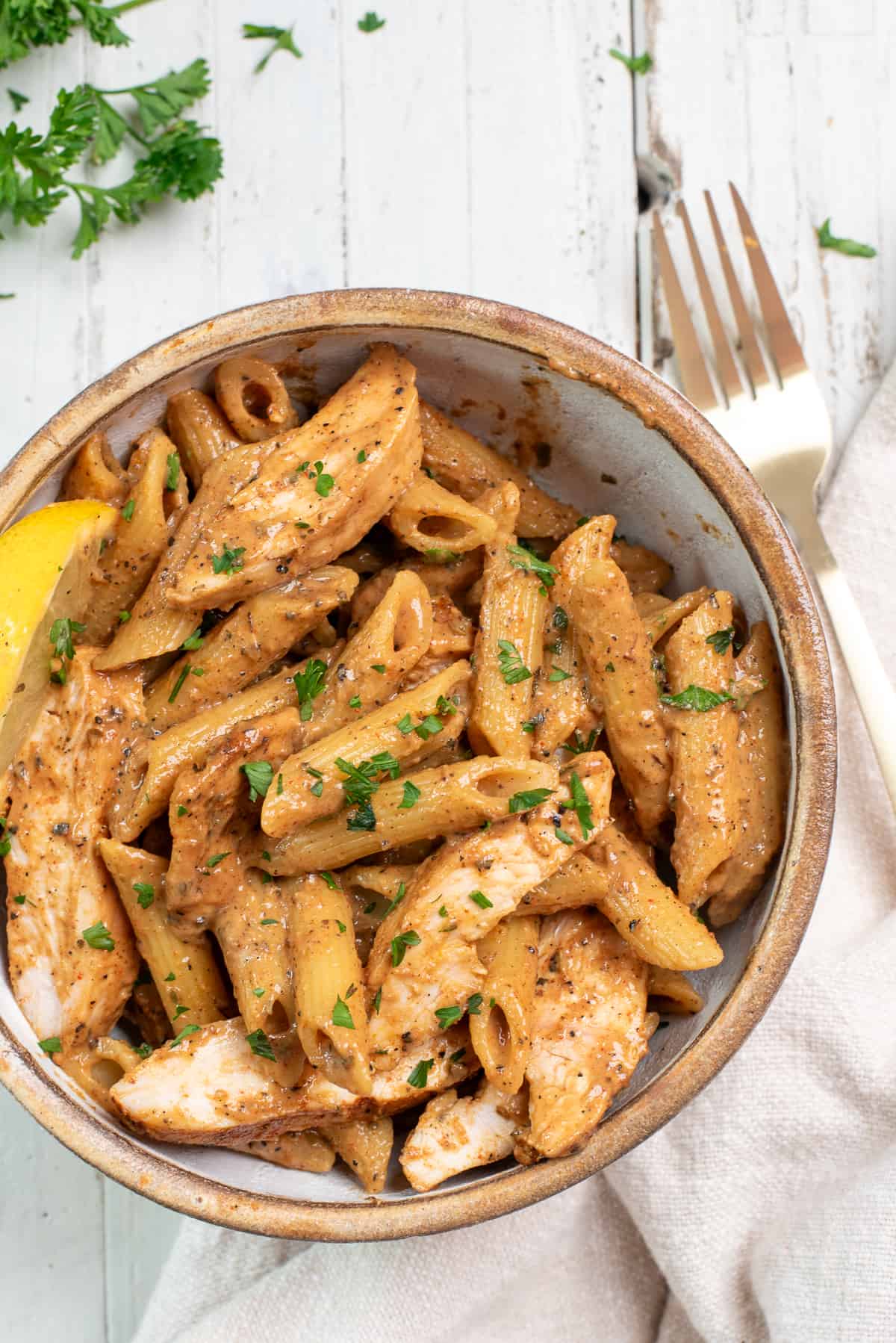 pasta in a beige bowl on a white background with a fork and a slice of lemon