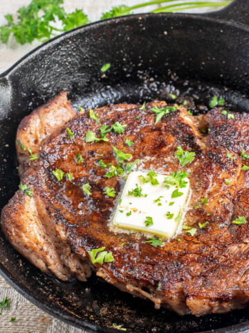 blackened ribeye steak with butter in skillet.